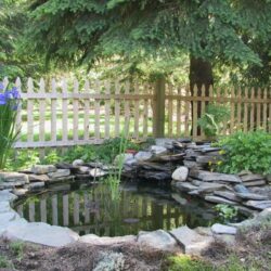 A rustic wooden fence featuring vertical slats with a weathered finish, set against a backdrop of dense green foliage, providing a charming boundary for a garden.