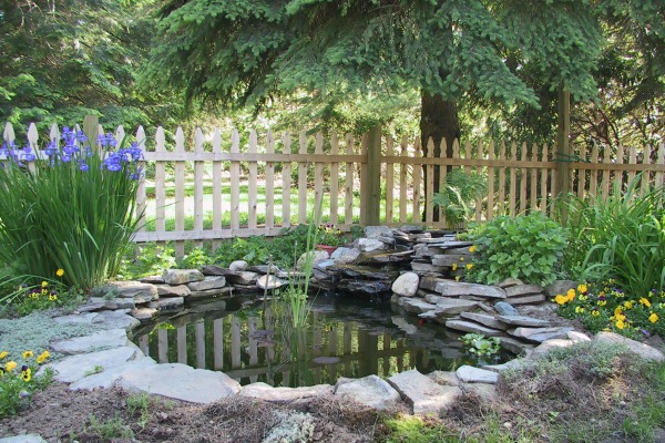 A rustic wooden fence featuring vertical slats with a weathered finish, set against a backdrop of dense green foliage, providing a charming boundary for a garden.