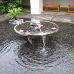 A large, dynamic fountain with powerful jets of water shooting upwards from a wide pool, creating a lively water display in a public park.