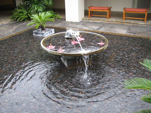 A large, dynamic fountain with powerful jets of water shooting upwards from a wide pool, creating a lively water display in a public park.