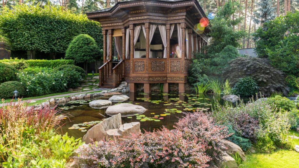 A quaint wooden house surrounded by a lush garden, featuring a serene pond at its center.