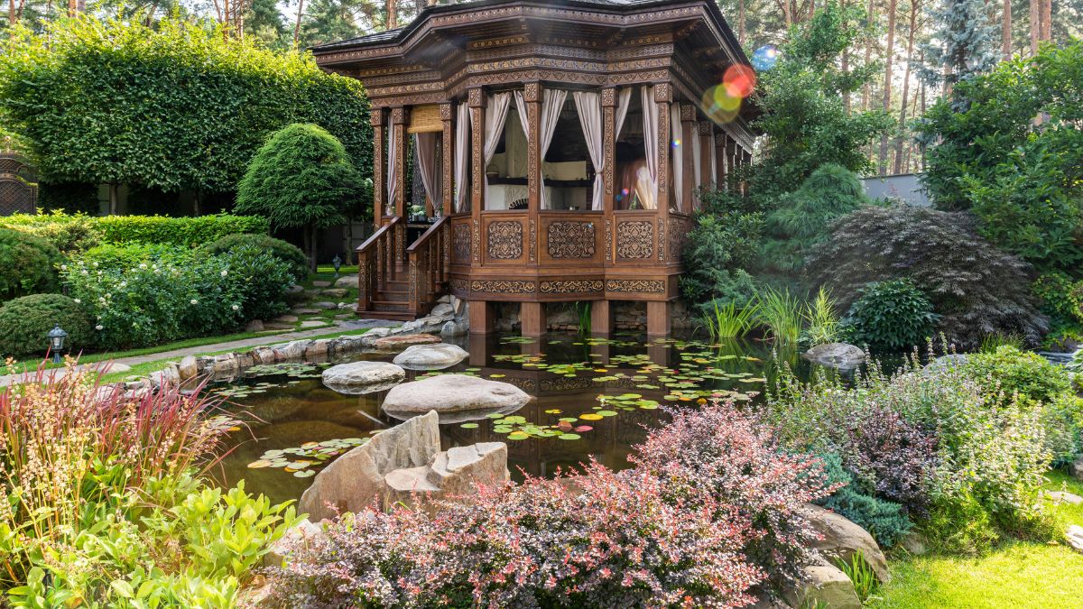 A quaint wooden house surrounded by a lush garden, featuring a serene pond at its center.