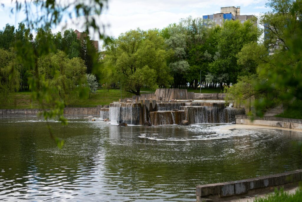 A serene pond featuring a waterfall, surrounded by lush greenery in a tranquil park setting.