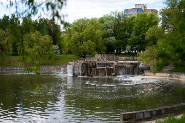 A serene pond featuring a waterfall, surrounded by lush greenery in a tranquil park setting.